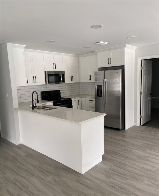 A kitchen features white cabinets, stainless steel appliances, a quartz island, and light wood-look flooring — 5008 PARADE STREET, TAMPA, FL