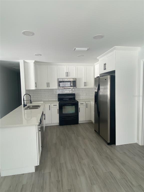 A modern kitchen features white cabinets, stainless steel appliances, a kitchen island, and gray flooring — 5008 PARADE STREET, TAMPA, FL