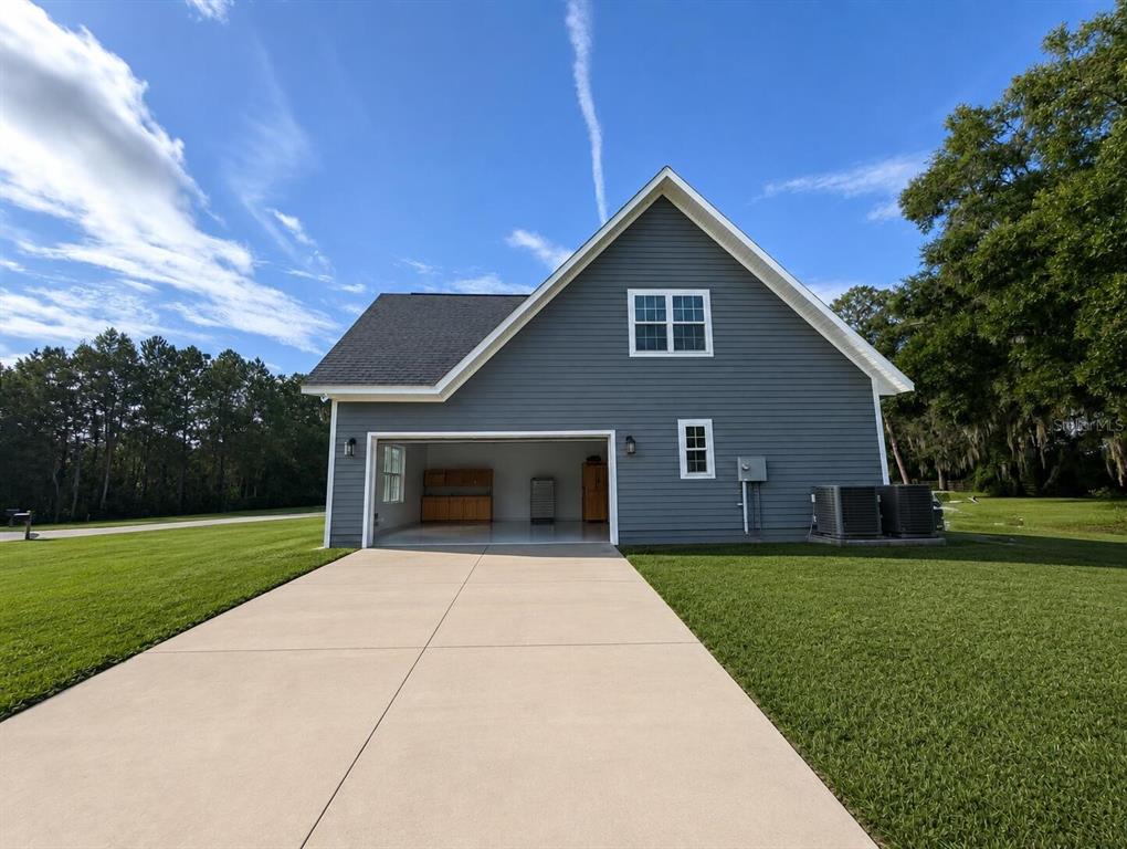 A gray-sided detached garage with an open bay, concrete driveway, and a second-story window — 841 NW 4TH AVENUE, WILLISTON, FL
