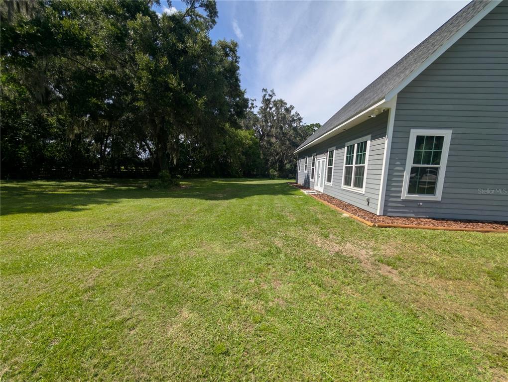 A side view of a gray-sided house with a large, grassy backyard and trees — 841 NW 4TH AVENUE, WILLISTON, FL