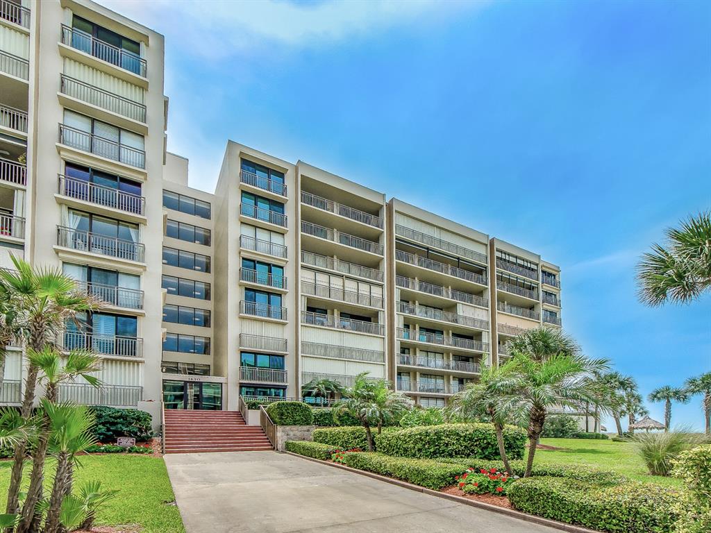 A multi-story apartment building features balconies, a concrete driveway, and landscaped grounds with palm trees — 1430 GULF BOULEVARD UNIT 110, CLEARWATER, FL