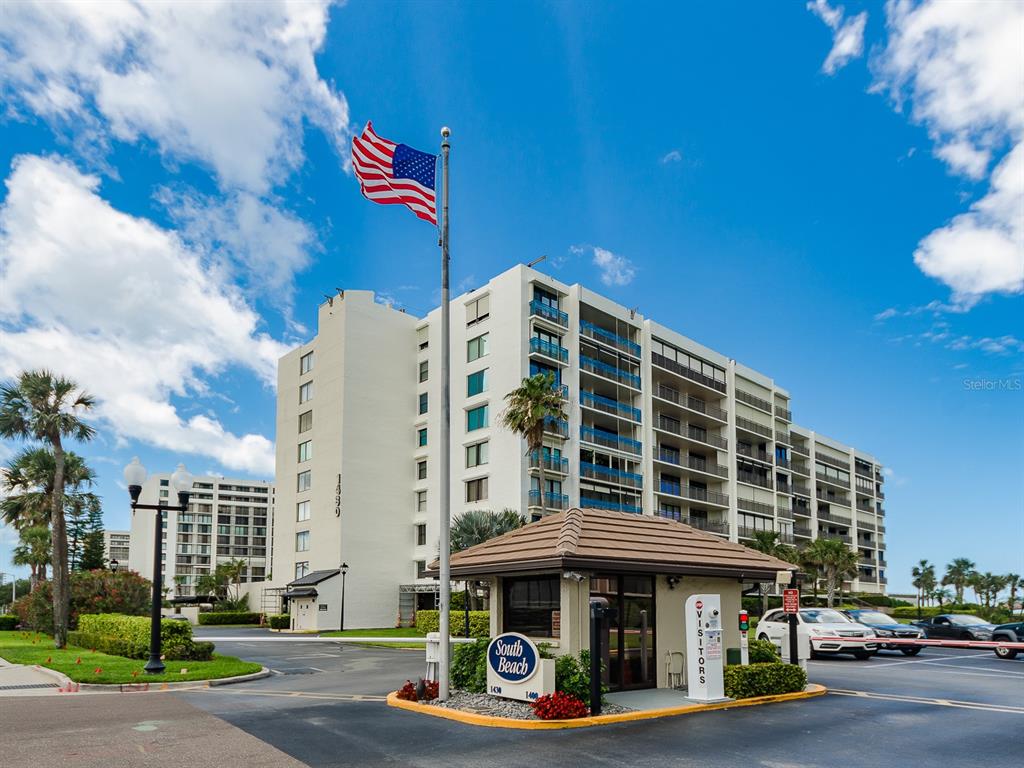 A multi-story residential building with a gated entrance, a flag, and a visitor kiosk — 1430 GULF BOULEVARD UNIT 110, CLEARWATER, FL