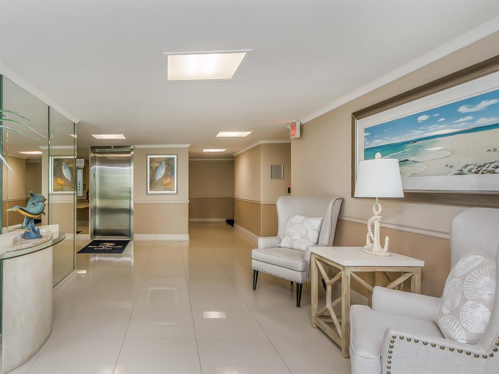 A bright lobby features a stainless steel elevator, tiled floors, and two upholstered armchairs — 1430 GULF BOULEVARD UNIT 110, CLEARWATER, FL