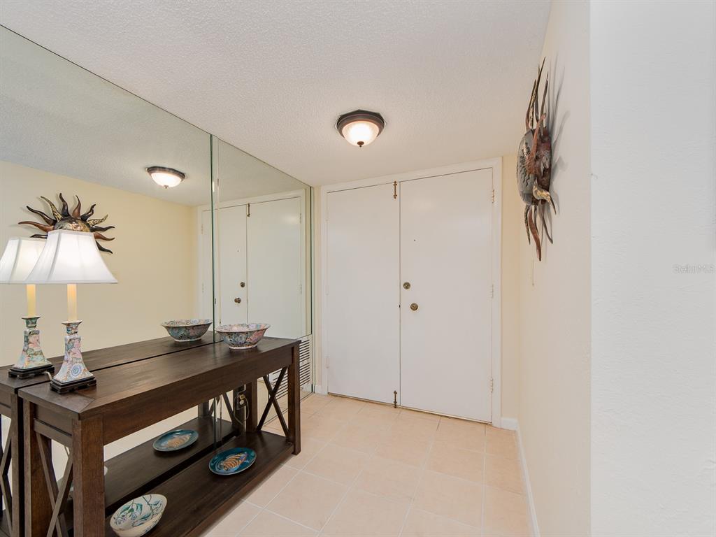 An entryway features a wooden console table, a large wall mirror, and double doors — 1430 GULF BOULEVARD UNIT 110, CLEARWATER, FL