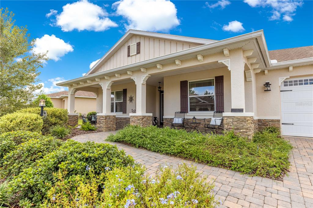 A single-story house with a stone-accented porch, paver walkway, and manicured landscaping under a blue sky — 9099 SW 89TH LOOP, OCALA, FL