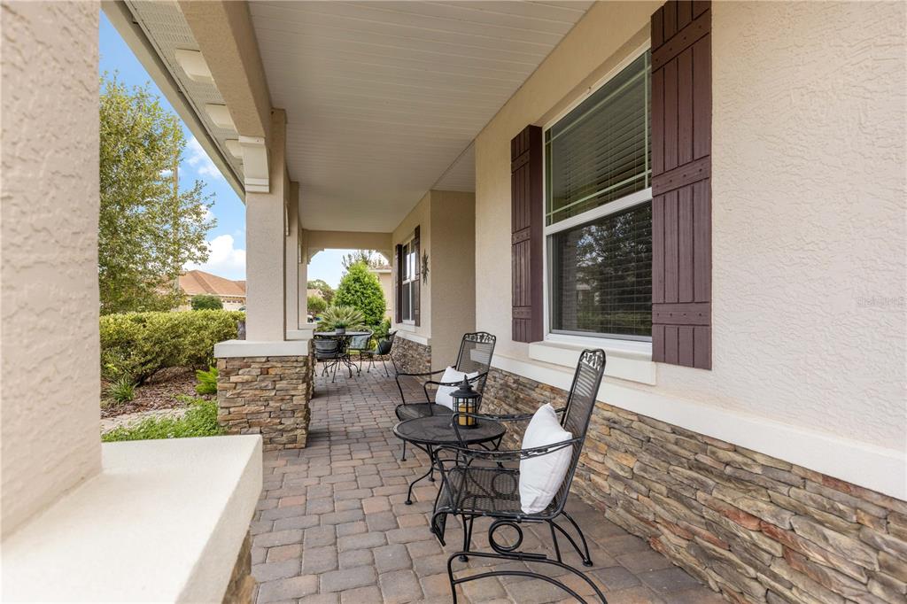 A covered front porch features stone accents, brick pavers, and outdoor seating — 9099 SW 89TH LOOP, OCALA, FL