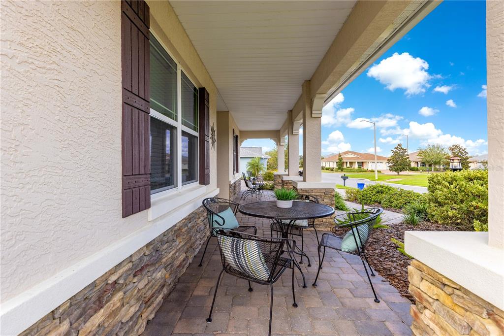 A covered stone-tiled porch features a metal patio table and chairs with cushions — 9099 SW 89TH LOOP, OCALA, FL