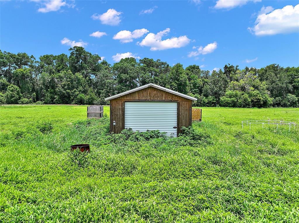 A small wooden shed with a white roll-up door sits in a grassy field — 15785 NW 33RD TERRACE, REDDICK, FL