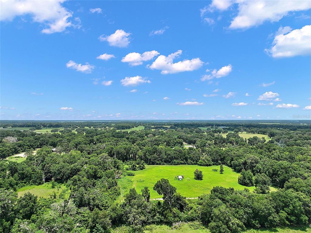 An aerial view shows a large, grassy clearing surrounded by dense forest under a blue sky — 15785 NW 33RD TERRACE, REDDICK, FL