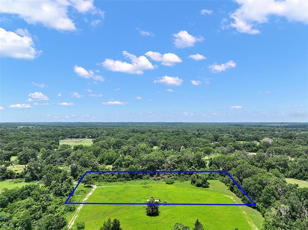 An aerial view shows a rectangular, fenced-in grassy field surrounded by dense green trees — 15785 NW 33RD TERRACE, REDDICK, FL