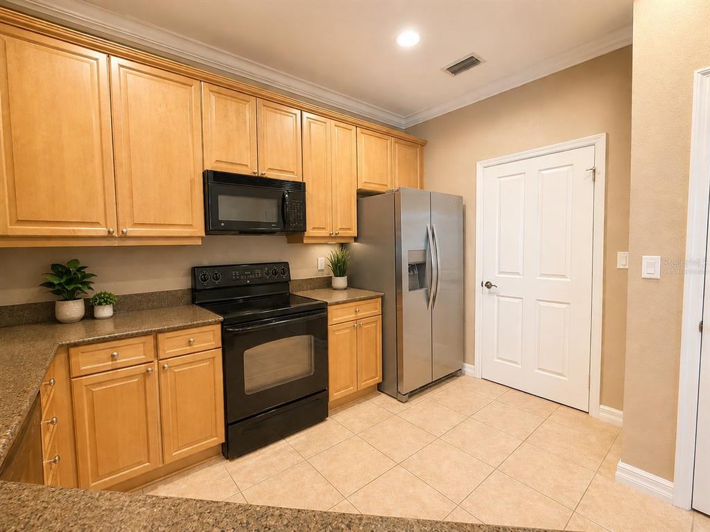 A kitchen featuring light wood cabinets, black appliances, a stainless steel refrigerator, and tiled flooring — 8168 BOAT HOOK LOOP UNIT 724, WINDERMERE, FL