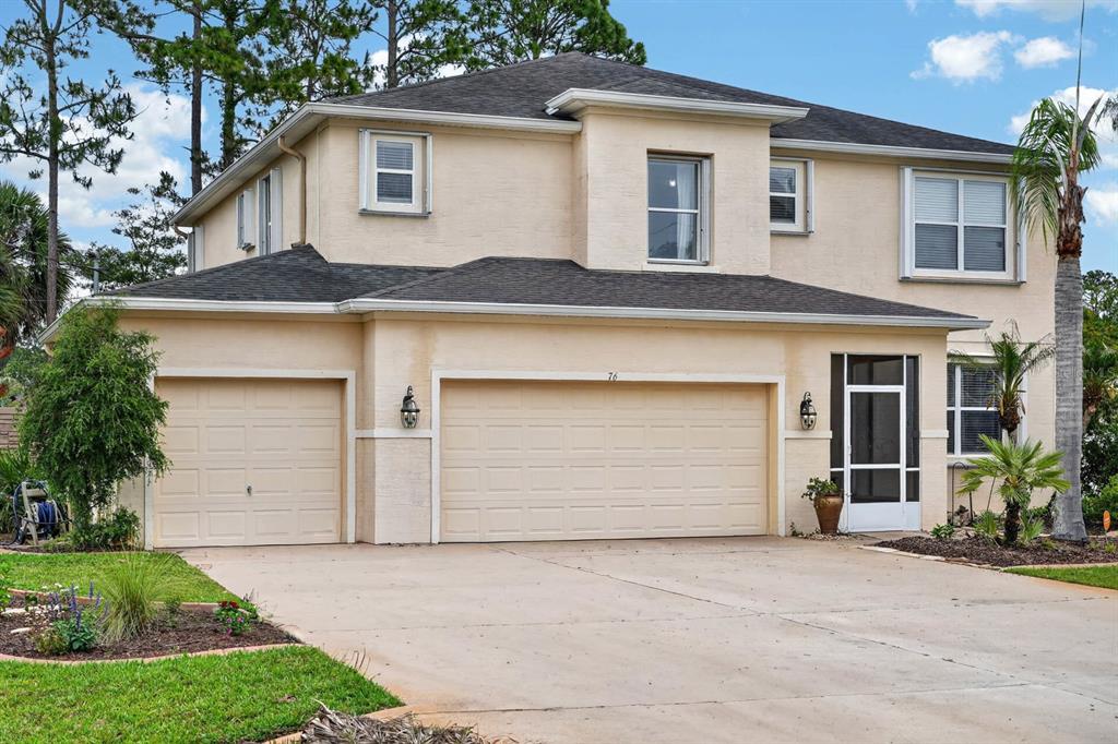 A two-story house with a three-car garage, beige stucco exterior, and a dark shingled roof — 76 UNIVERSAL TRAIL, PALM COAST, FL
