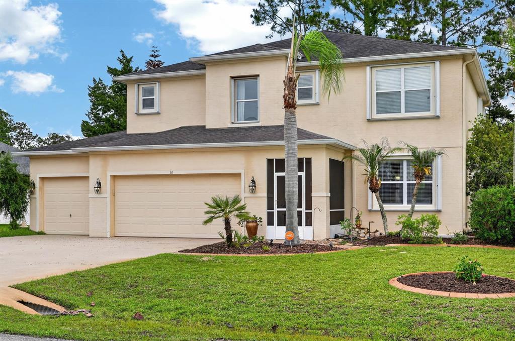A two-story beige house with a three-car garage, a screened entryway, and a front lawn — 76 UNIVERSAL TRAIL, PALM COAST, FL