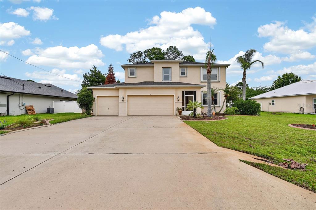 A two-story suburban house with a beige stucco exterior, a three-car garage, and a driveway — 76 UNIVERSAL TRAIL, PALM COAST, FL
