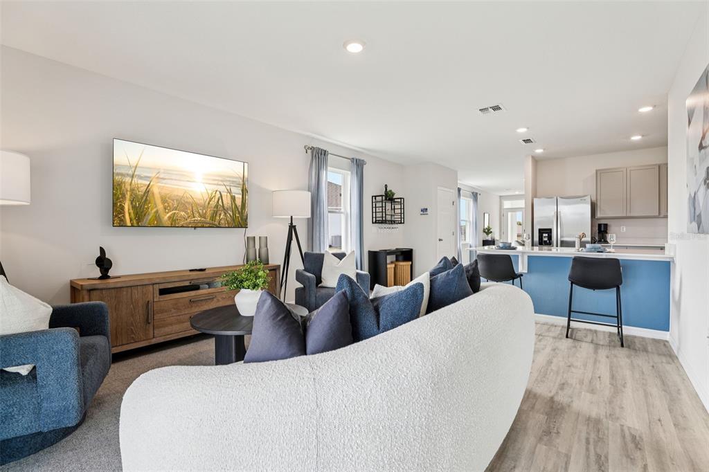 A living room with a curved sofa, blue armchairs, and an open kitchen with bar seating — 4049 GIORGIO DRIVE, WINTER HAVEN, FL