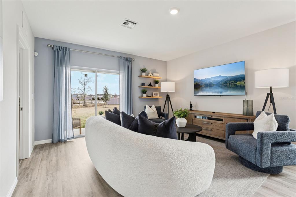 A living room features a curved white sofa, blue armchairs, and a sliding glass door — 4049 GIORGIO DRIVE, WINTER HAVEN, FL
