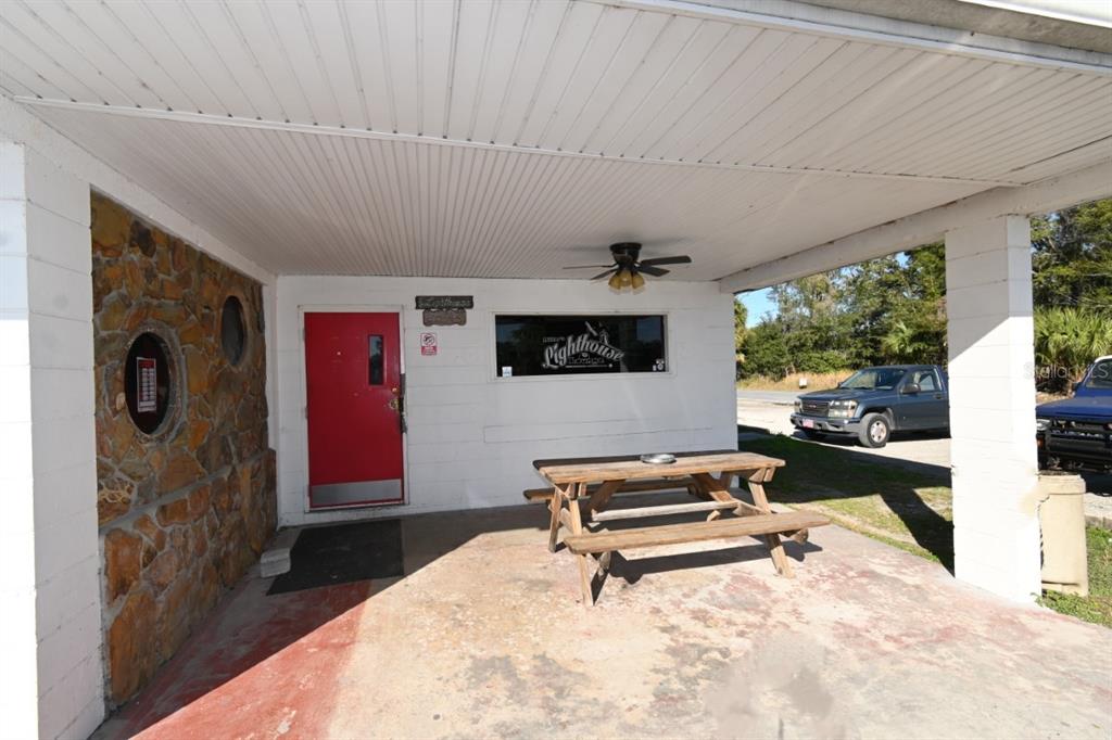 A red door and a wooden picnic table are on the covered porch of a building — 5025 TREIMAN BOULEVARD, DADE CITY, FL
