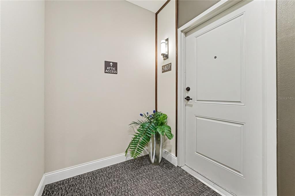 A hallway entrance features a white door, a potted plant, and an attic access sign — 7505 LAUREATE BOULEVARD UNIT 2407, ORLANDO, FL
