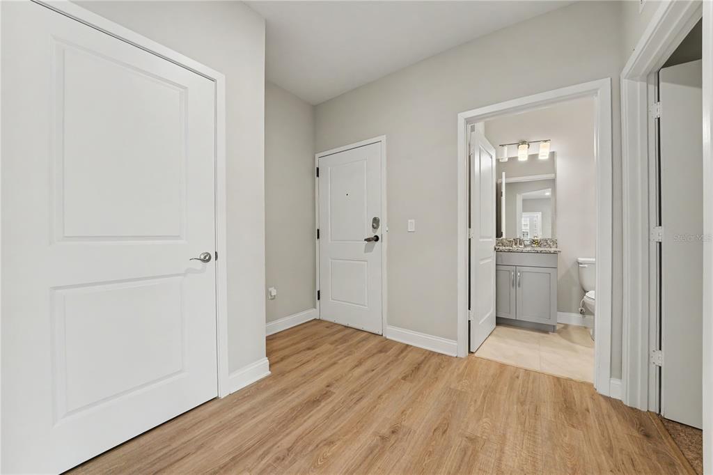 A hallway with wood-look flooring, white doors, and an open doorway leading to a bathroom — 7505 LAUREATE BOULEVARD UNIT 2407, ORLANDO, FL