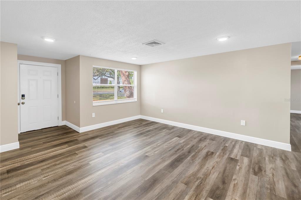 An empty living room features light beige walls, wood-look flooring, a window, and recessed lighting — 518 62ND AVENUE NE, ST PETERSBURG, FL
