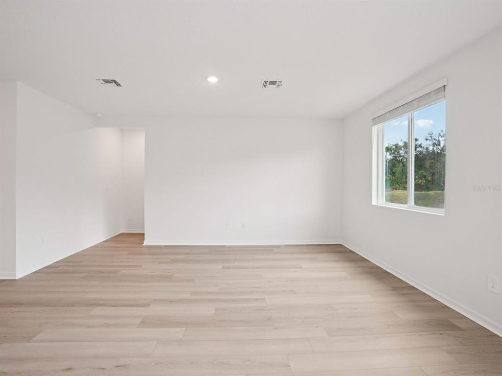 An empty room with white walls, light wood-look flooring, and a window overlooking trees — 17661 OLIVE THORN DRIVE, BROOKSVILLE, FL