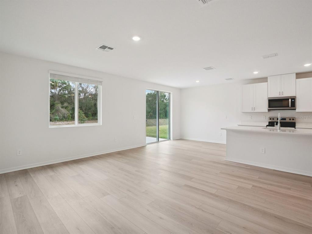 An open-concept living area features light wood-look flooring, white walls, and a modern kitchen — 17661 OLIVE THORN DRIVE, BROOKSVILLE, FL