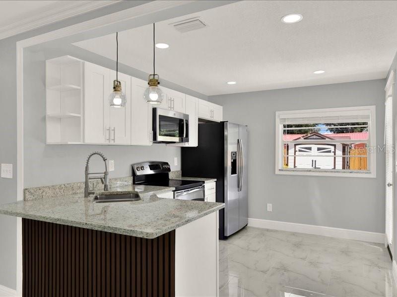 A kitchen with white cabinets, granite countertops, stainless steel appliances, and a dark wood island — 2712 E 99TH AVENUE, TAMPA, FL