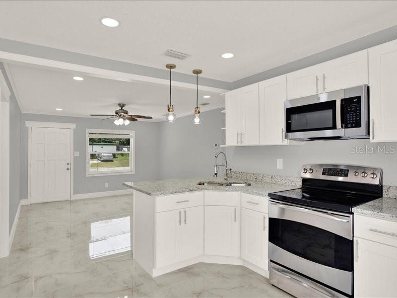 A kitchen with white cabinets, granite countertops, stainless steel appliances, and light-colored tile flooring — 2712 E 99TH AVENUE, TAMPA, FL
