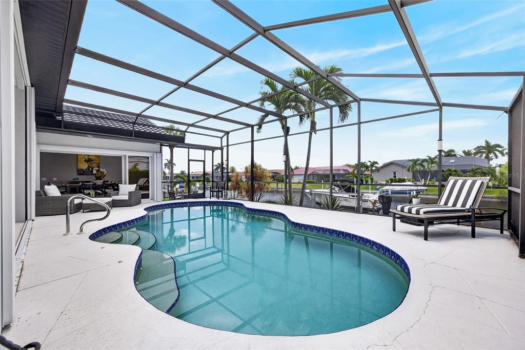 A screened-in pool patio features a kidney-shaped pool, lounge chairs, and a view of a canal — 1552 AQUI ESTA DRIVE, PUNTA GORDA, FL