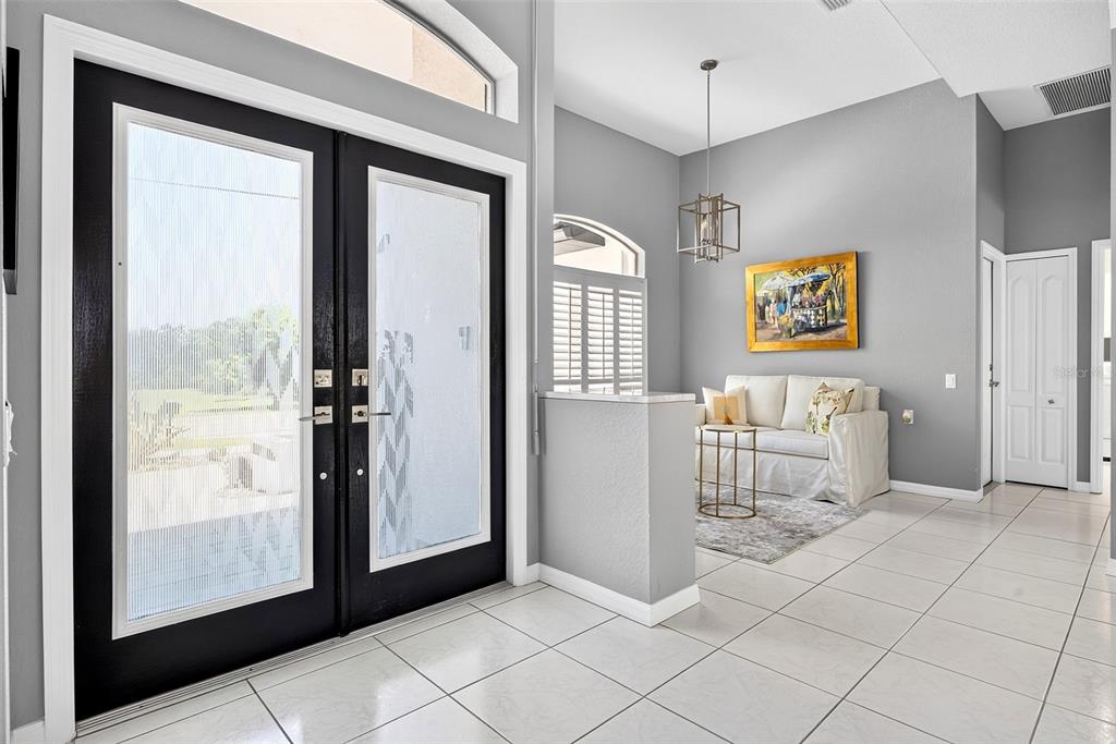 A bright entryway features black double doors, white tile flooring, and a small seating area — 1552 AQUI ESTA DRIVE, PUNTA GORDA, FL