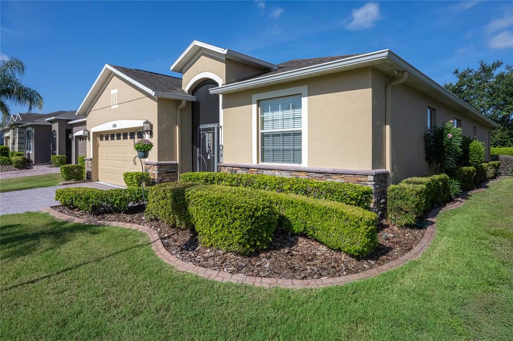 A single-story suburban house with a tan stucco exterior, a two-car garage, and manicured landscaping — 3650 LIMESTONE STREET, CLERMONT, FL