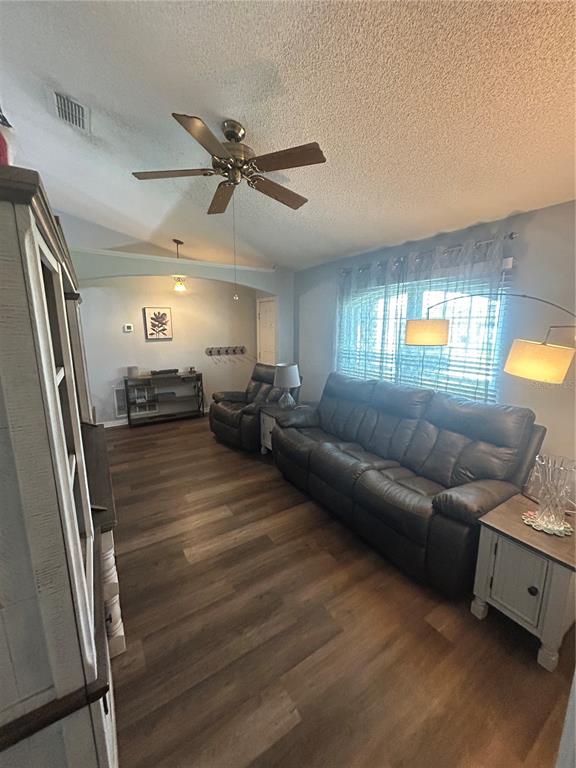 A living room features wood-look flooring, a dark leather sofa, a ceiling fan, and an archway — 3243 BRETTON WOODS TERRACE, DELTONA, FL
