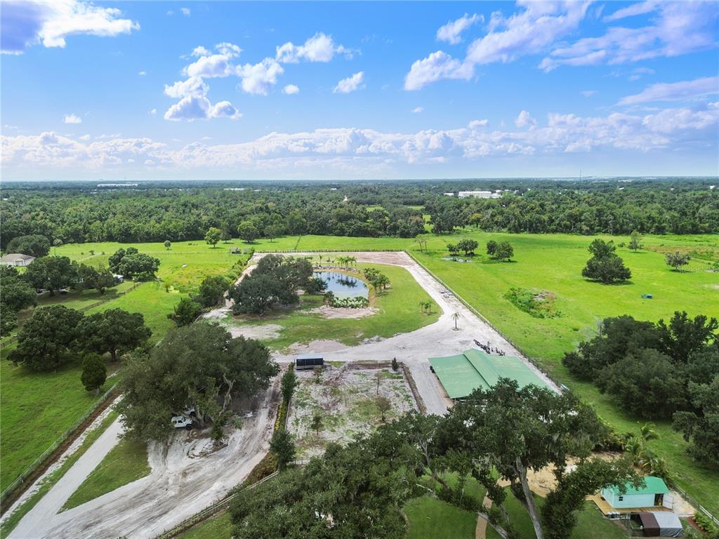 A wooden dock with a blue chair sits beside a pond covered in aquatic plants — 5925 SPENCER PARRISH ROAD, PARRISH, FL