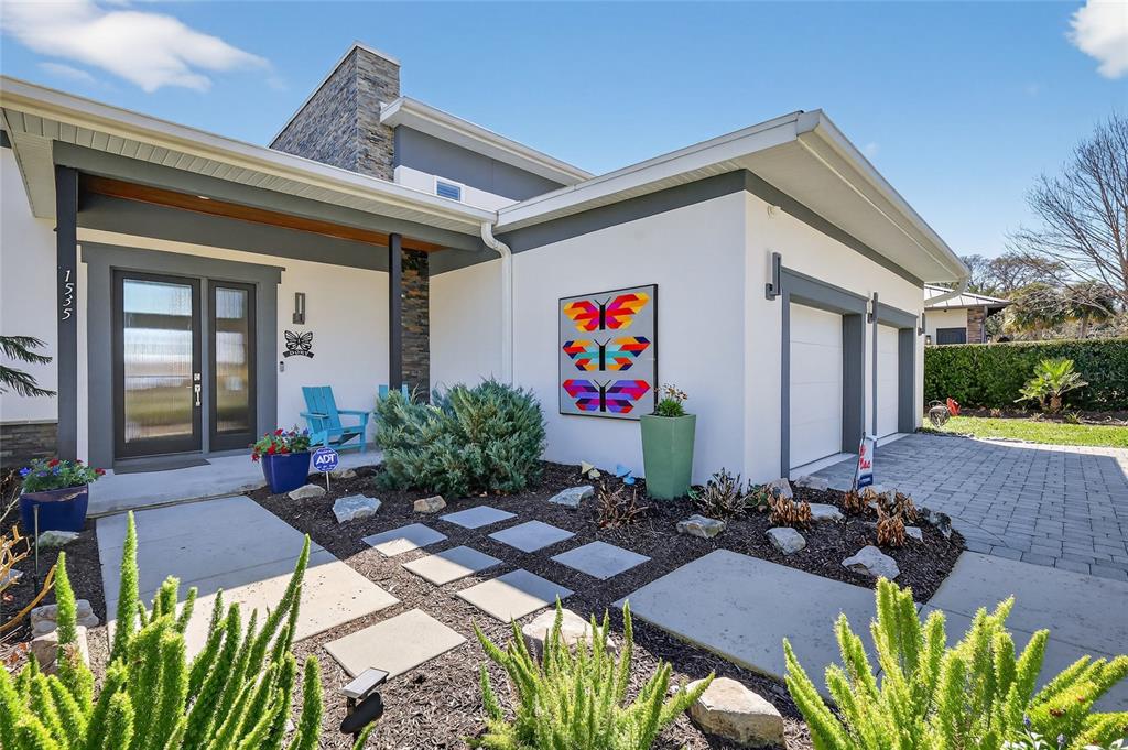 A modern house exterior features a stone chimney, a paved driveway, and colorful butterfly art — 1535 SUNSET CIRCLE, MOUNT DORA, FL