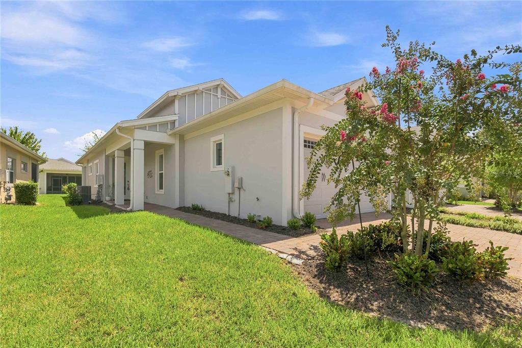 A side view of a light-colored house with a paved walkway and a flowering tree — 2374 DATURA LOOP, ST CLOUD, FL