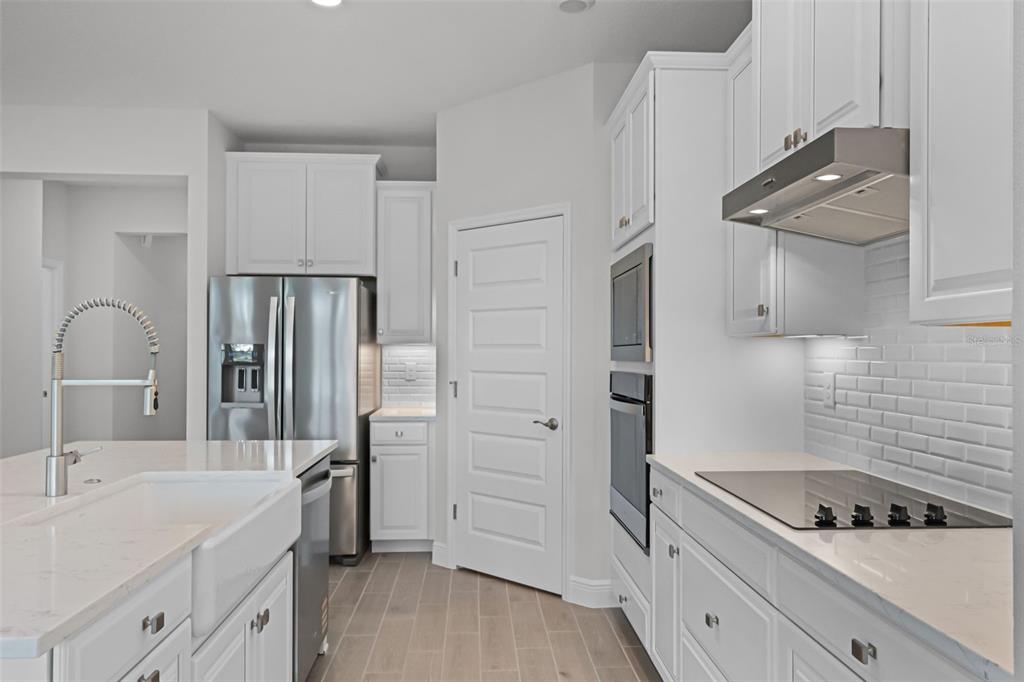 A modern kitchen features white cabinetry, stainless steel appliances, a farmhouse sink, and quartz countertops — 11923 SHINE VIEW LANE, WINTER GARDEN, FL