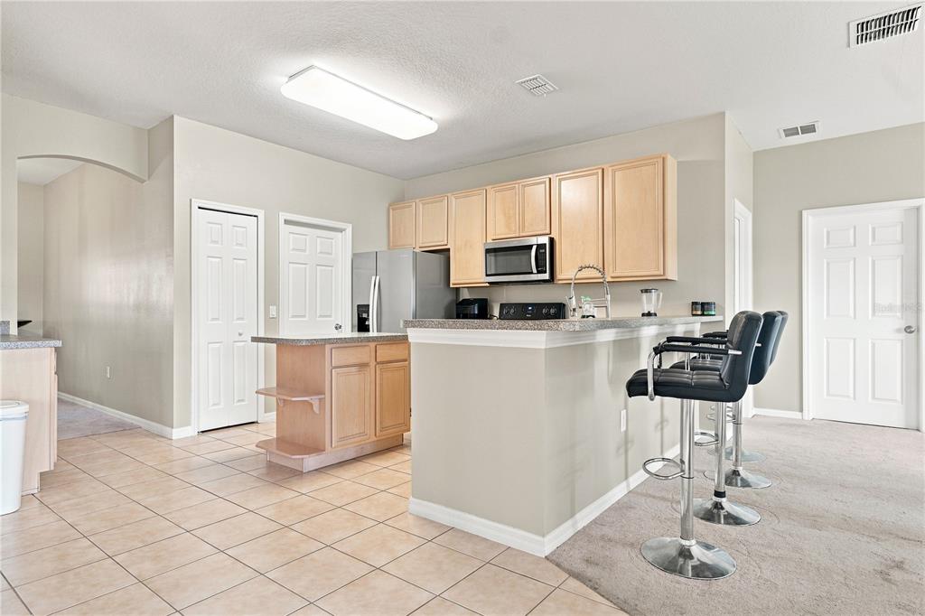 A kitchen with light wood cabinets, a breakfast bar, and tile flooring next to carpet — 3616 VALLEYVIEW DRIVE, KISSIMMEE, FL
