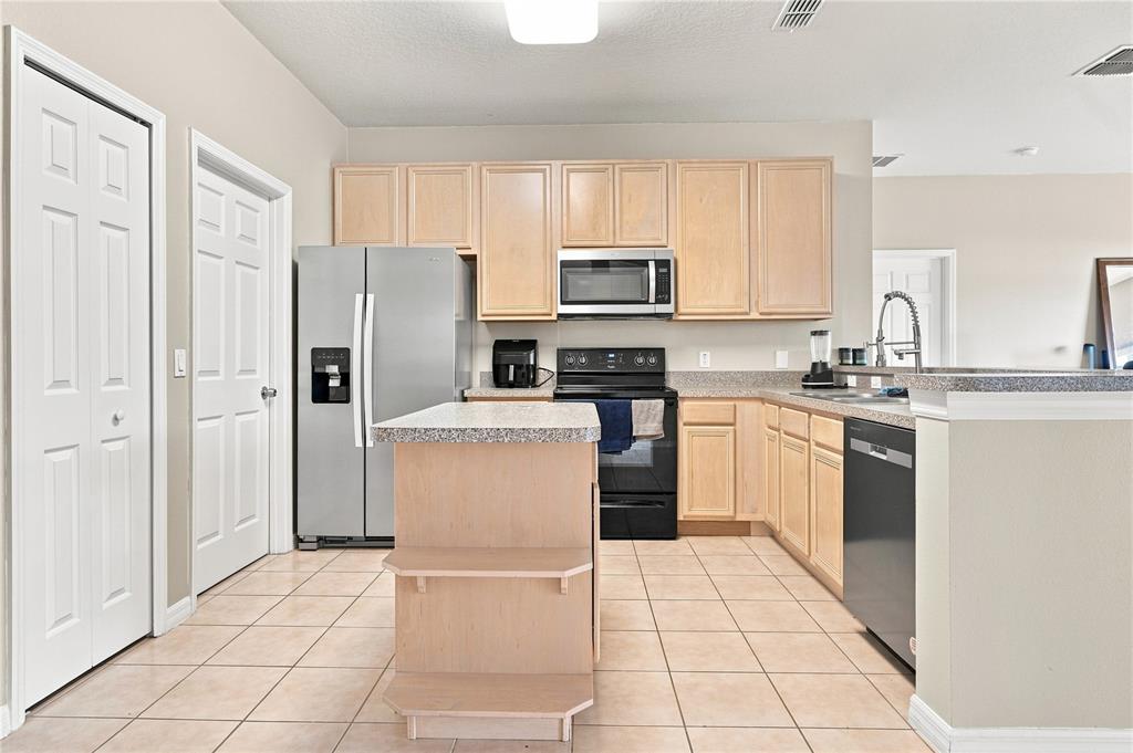 A kitchen features light wood cabinets, stainless steel appliances, a center island, and tile flooring — 3616 VALLEYVIEW DRIVE, KISSIMMEE, FL