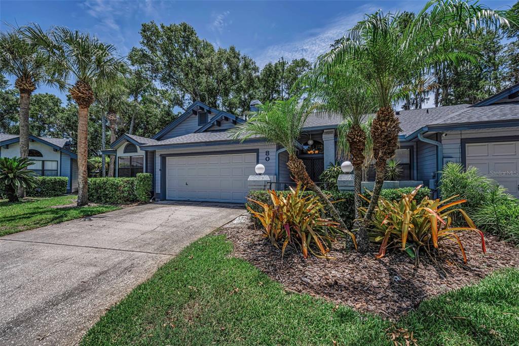A single-story house with a two-car garage, palm trees, and landscaping under a blue sky — 80 SUMMERWINDS LANE, OLDSMAR, FL