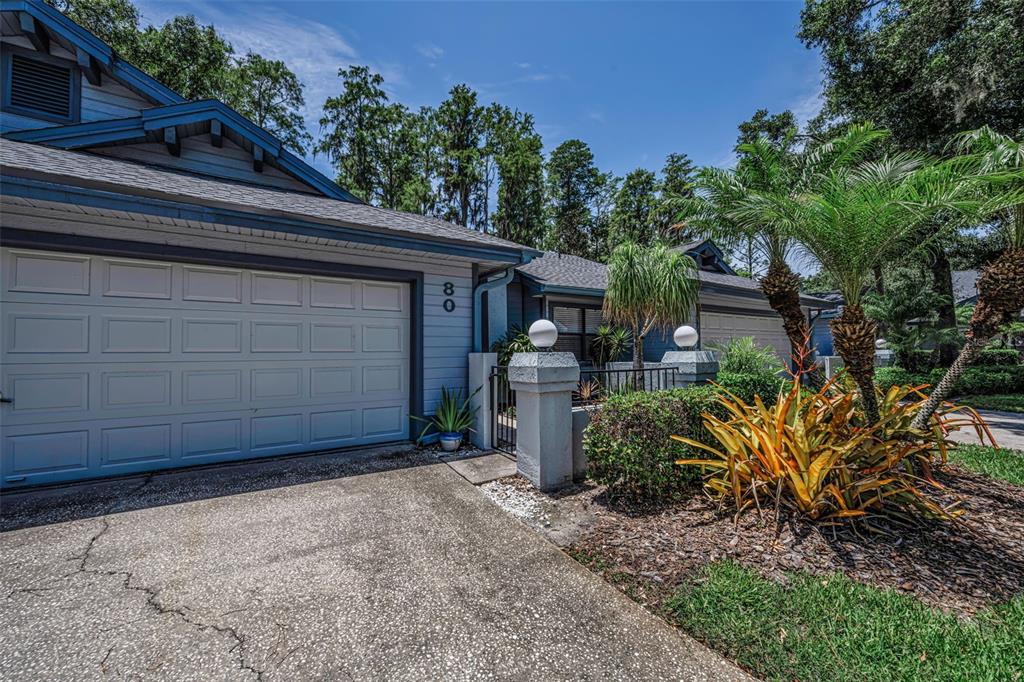 A blue house exterior features a garage, a concrete driveway, and a landscaped front yard — 80 SUMMERWINDS LANE, OLDSMAR, FL
