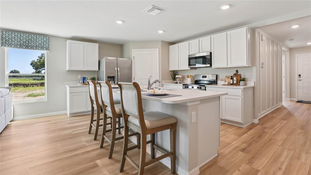 A kitchen features white cabinets, a central island with three chairs, and light wood flooring — 2074 NE 28TH PLACE, OCALA, FL
