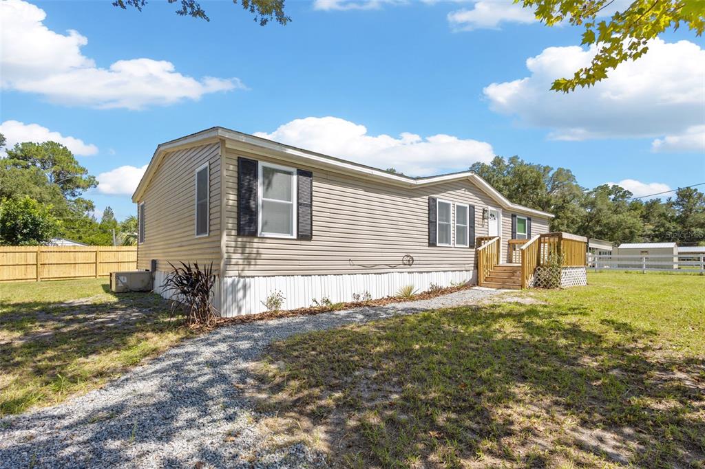 A beige mobile home with a gravel driveway and a wooden deck under a blue sky — 2691 NW 74TH TERRACE, CHIEFLAND, FL