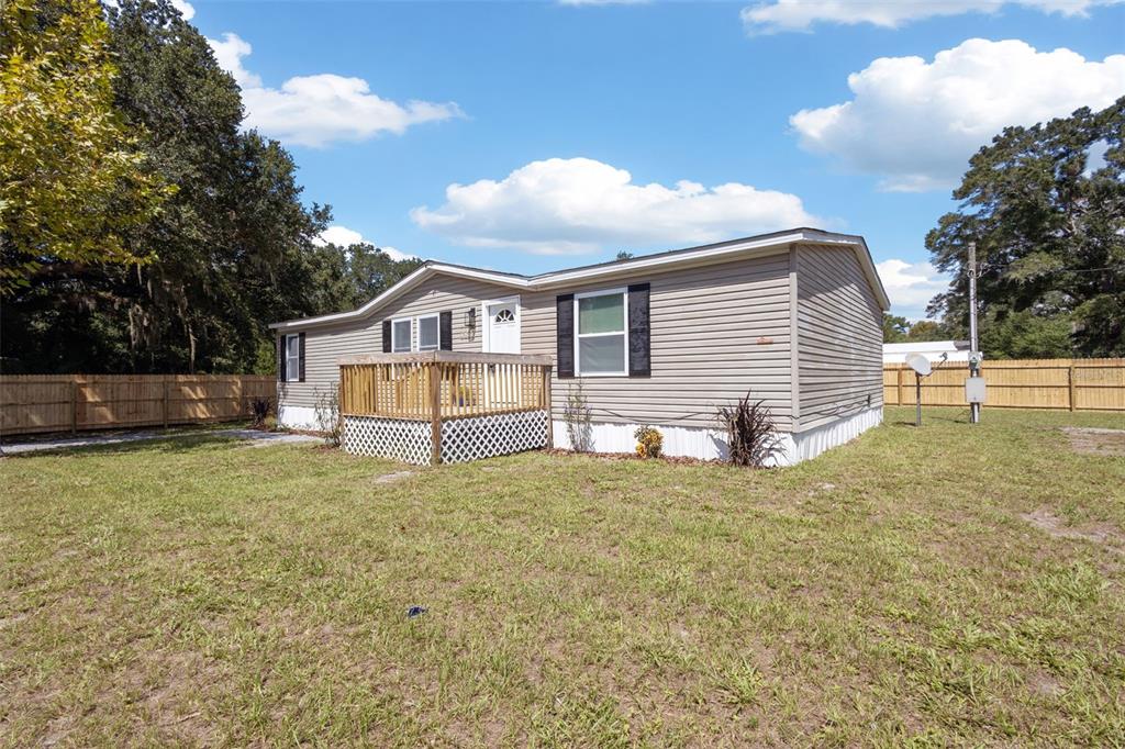 A single-story manufactured home with light siding, a wooden deck, and a fenced yard — 2691 NW 74TH TERRACE, CHIEFLAND, FL
