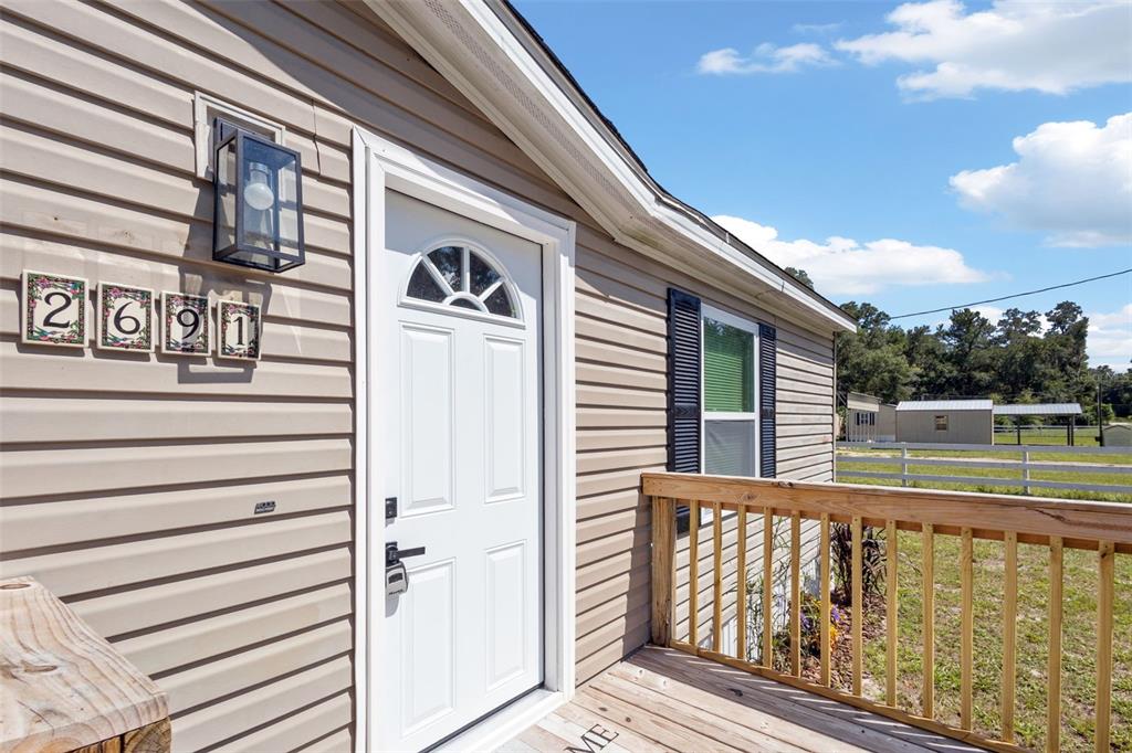 The exterior of a house features beige vinyl siding, a white front door, and a wooden porch — 2691 NW 74TH TERRACE, CHIEFLAND, FL