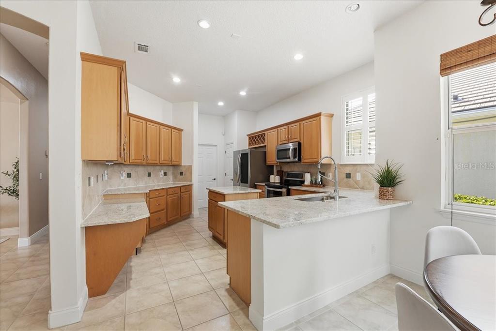 A kitchen features light wood cabinets, granite countertops, stainless steel appliances, and a central island — 10926 WOODCHASE CIRCLE, ORLANDO, FL