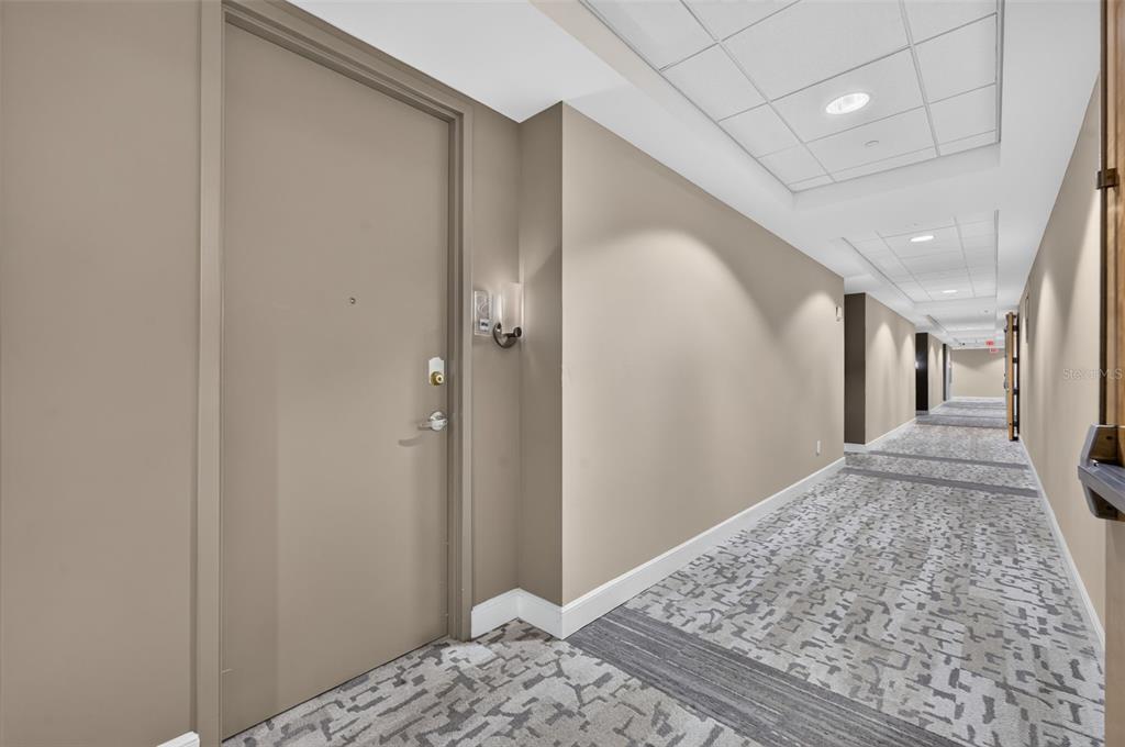 A long hallway features beige walls, a patterned carpet, and a closed door — 101 S EOLA DRIVE UNIT 1016, ORLANDO, FL