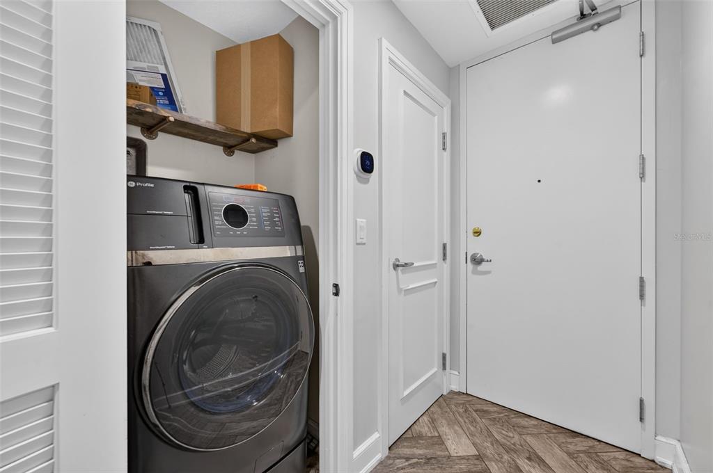 A laundry closet with a front-loading washer sits next to a white door and entryway — 101 S EOLA DRIVE UNIT 1016, ORLANDO, FL