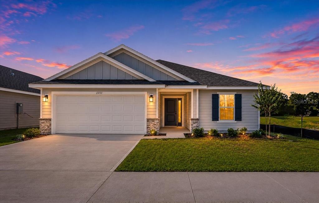 A single-story suburban house with a two-car garage and light gray siding at sunset — 13711 NW 150TH CIRCLE, ALACHUA, FL