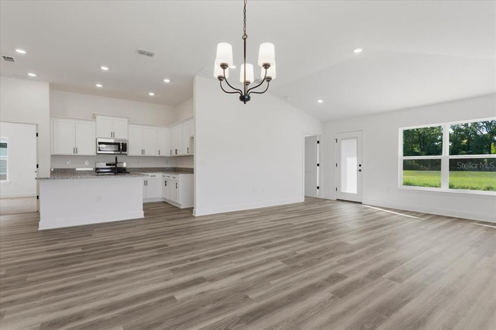 An open-concept living area features white cabinets, granite countertops, and light wood-look flooring — 13711 NW 150TH CIRCLE, ALACHUA, FL