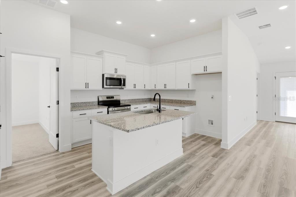 A kitchen with white cabinets, granite countertops, a center island, and light wood-look flooring — 13711 NW 150TH CIRCLE, ALACHUA, FL